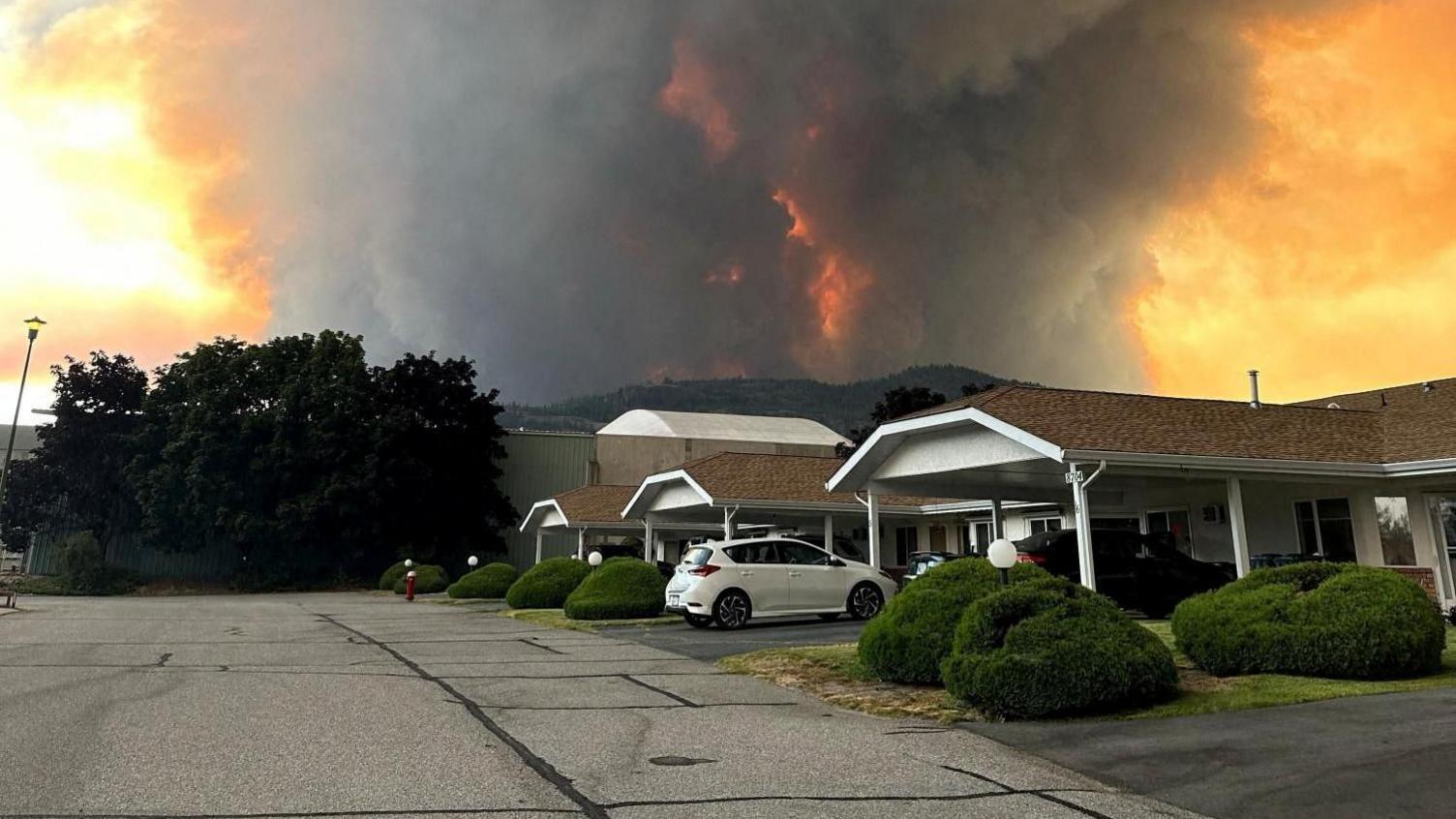 Grey and orange smoke rising behind a row of homes in Summerland, BC